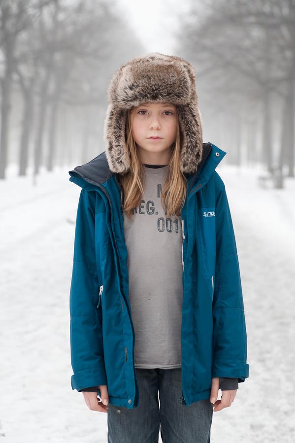 A photo of a girl who stands on a snowy street with a fur hat and winter jacket