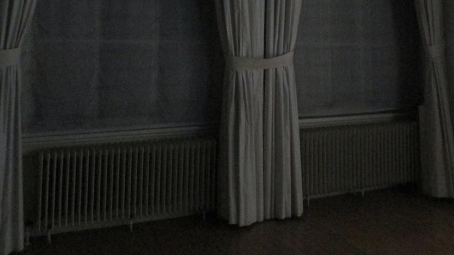 Video still of a dark room, long curtains hanging on the wall
