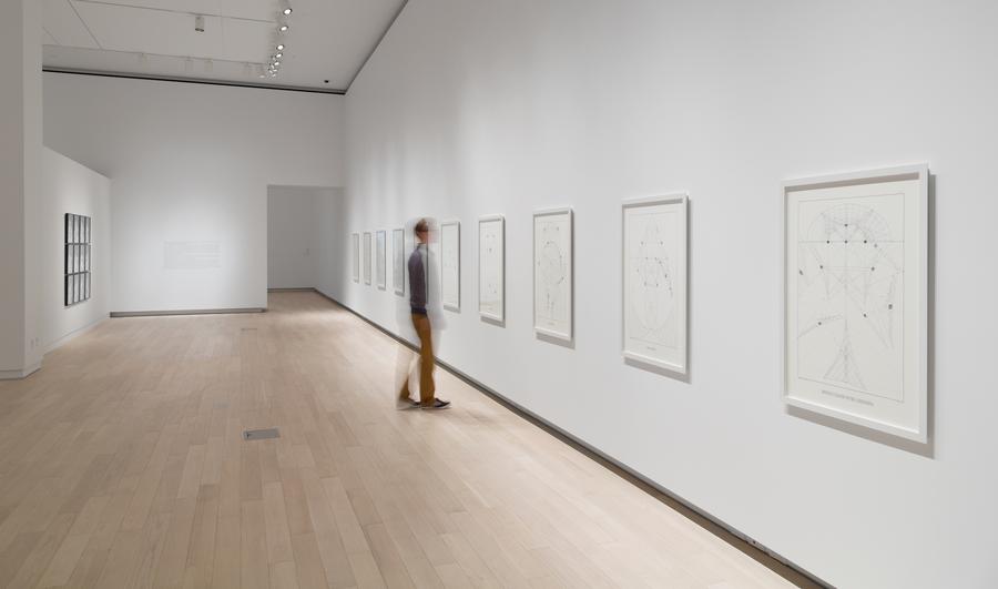 A man examines large white prints in the gallery