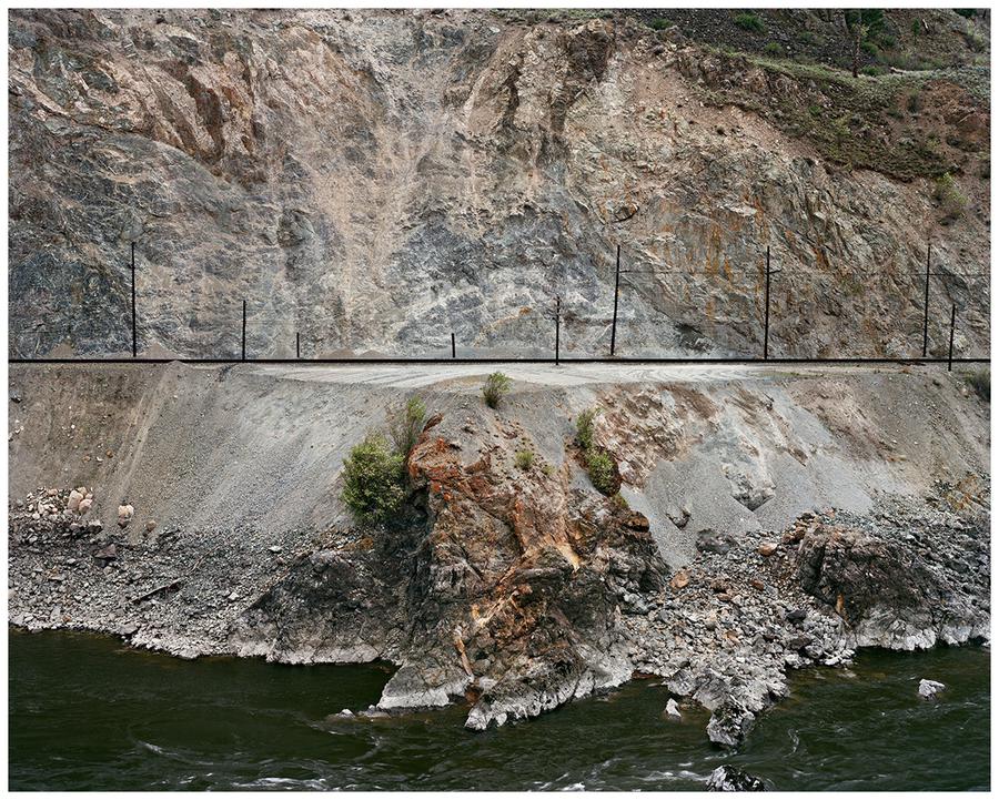 Photograph by Edward Burtynsky. A railway line cut into a mountain side.