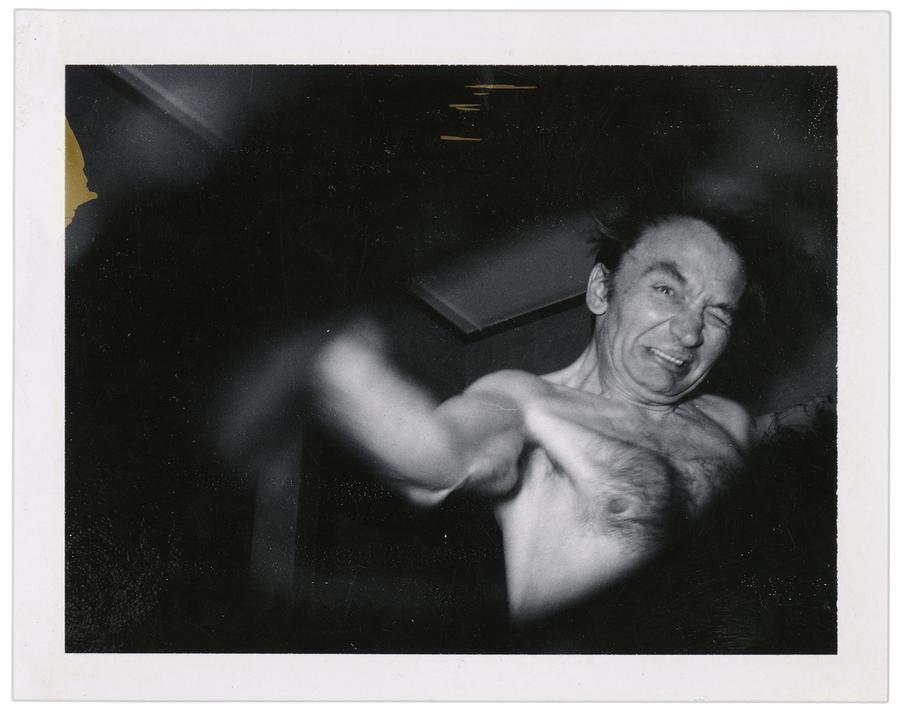 shirtless man, arm outstretched to lens, strained expression