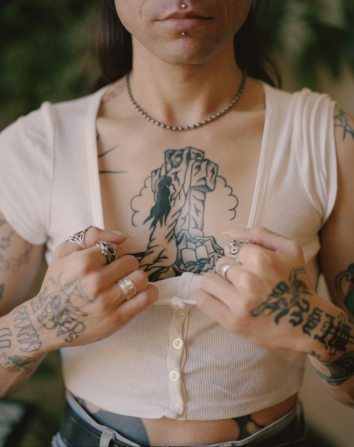 Person in white button up crop top pulls shirt collar down to reveal chest tattoo