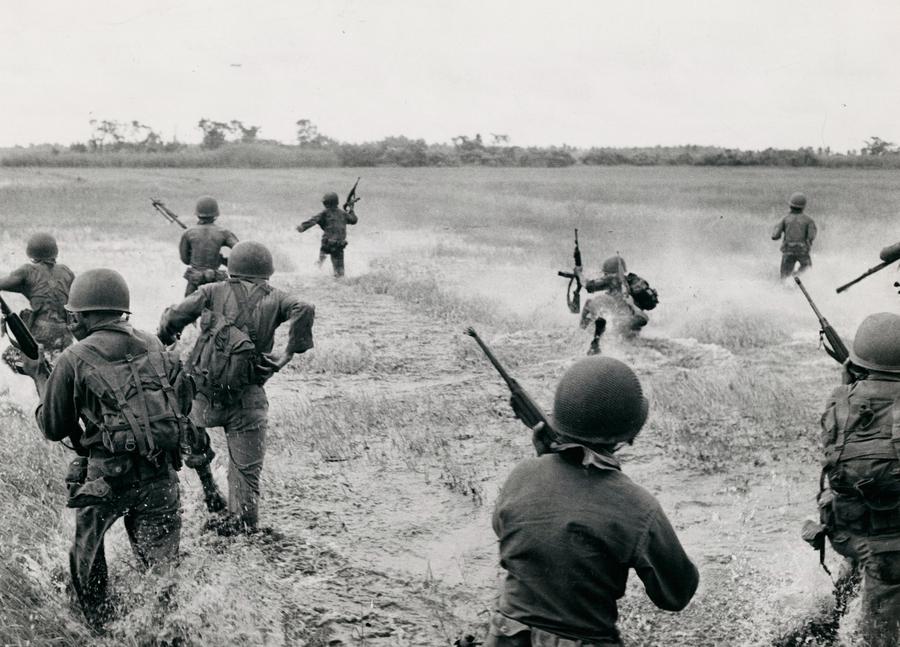 A group of soldiers with guns run through a field