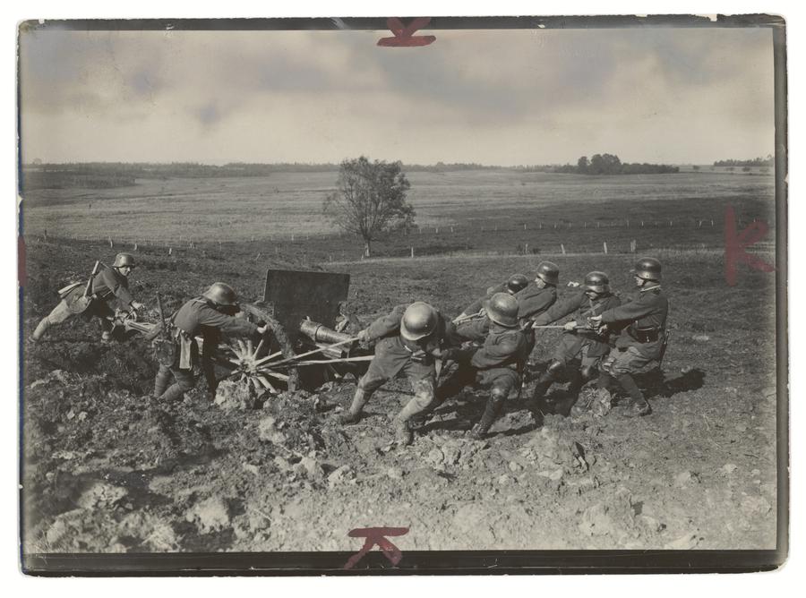 A group of soldiers work to pull a cart out of the mud