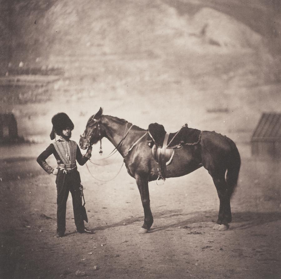 A man wearing a fur hat reaching out to his horse