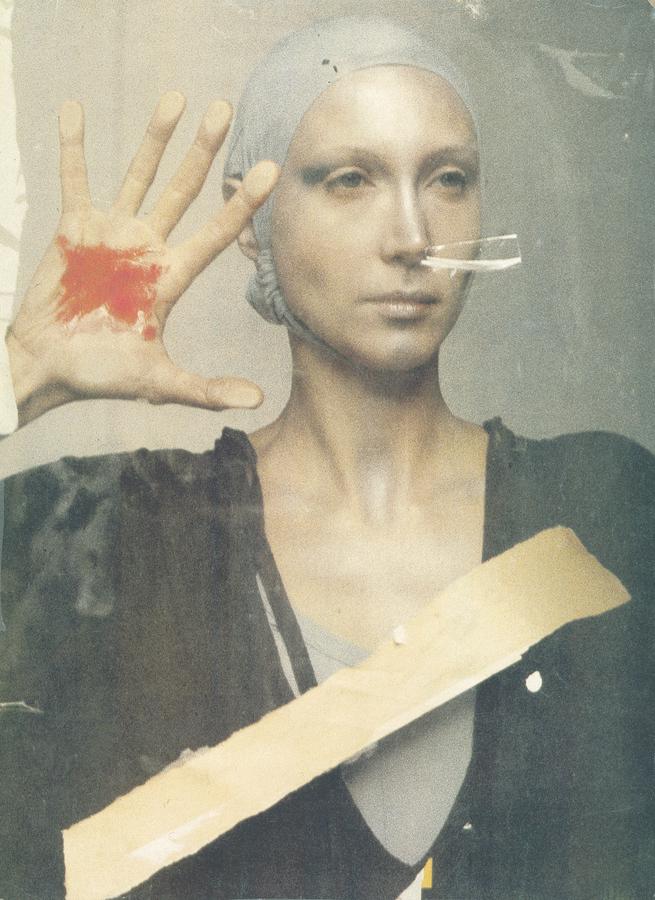 A white woman wearing a head wrap and a drapey black garment holds open her bloodied palm
