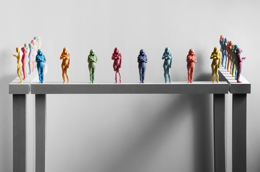 Multiple miniature colourful figurines of women texting are posed on a beam