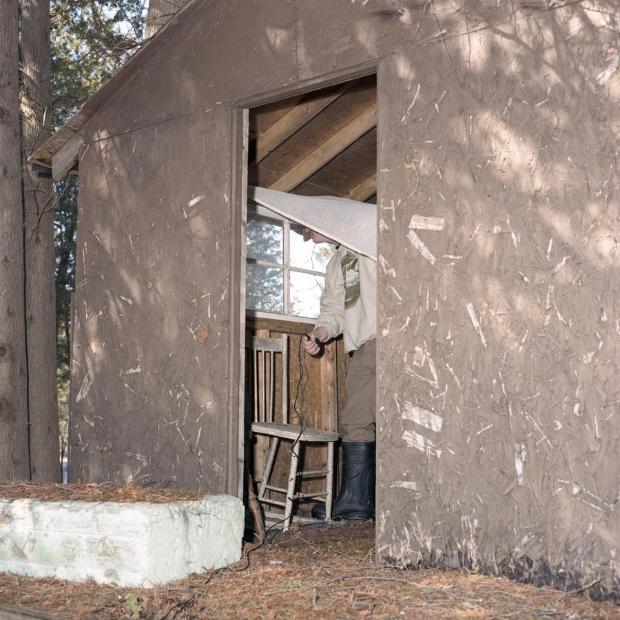 A person stands inside a wooden structure, partially visibile from the open doorway