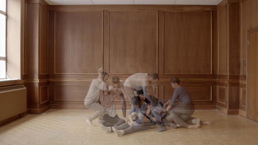 7 semi-transparent people holding each other in a large empty room