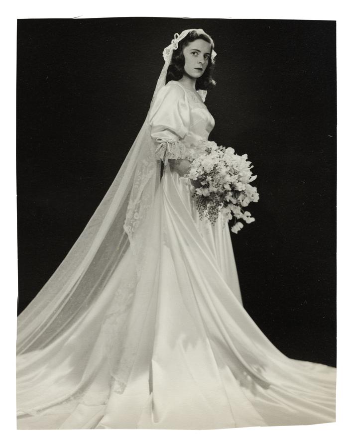 veiled bride stands and poses for a studio portrait photo, bouquet in hand.