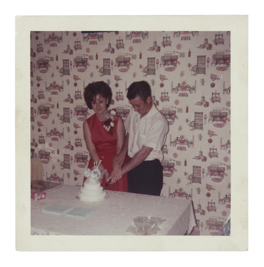 man and woman cut a three-tiered wedding cake with hands clasped together.