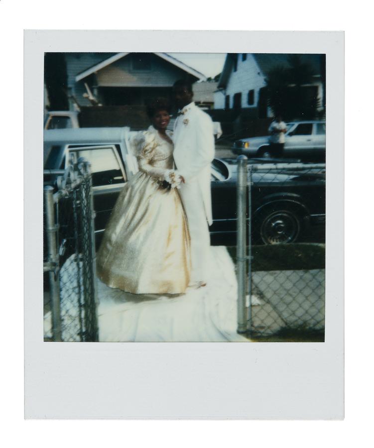 Black bride and groom stand posed at the end of their front of house walkway, by the lawn fence.