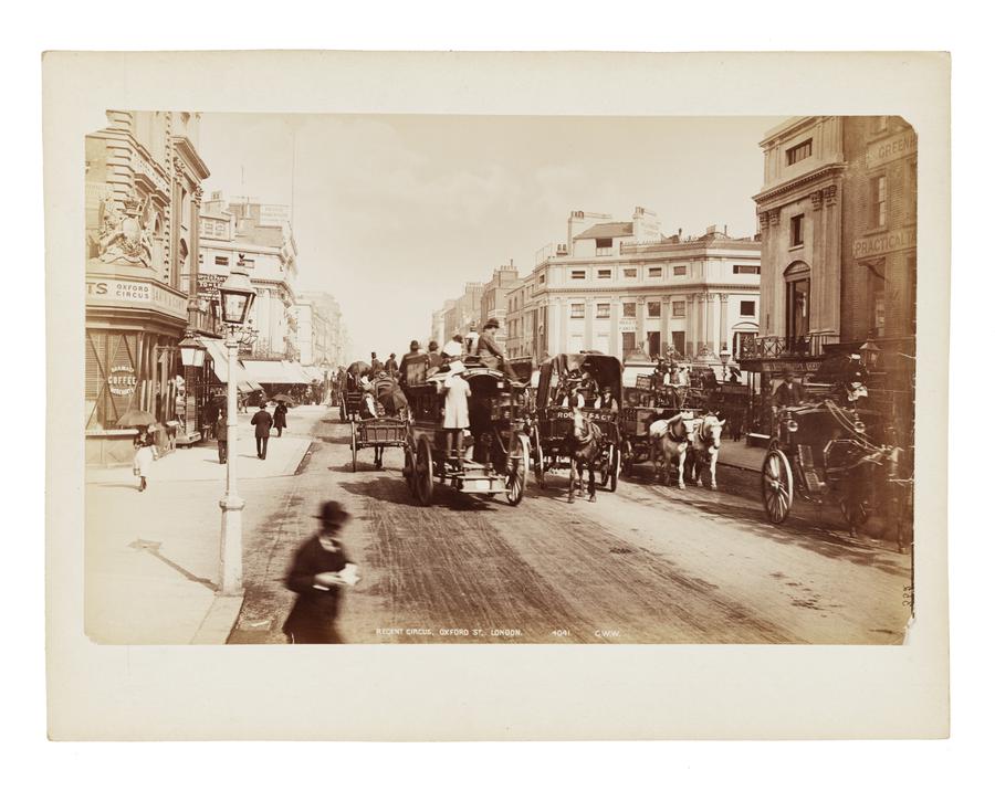 A 19th century street scene in London England, with horse drawn wagons and people