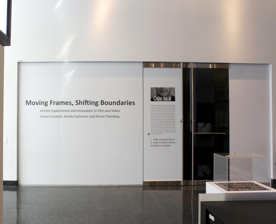 White door frame with text that reads "moving frames, shifting boundaries, artistic experiments and innovation in film and video, guest curators Gerda Cammaer and Pierre Tremblay"