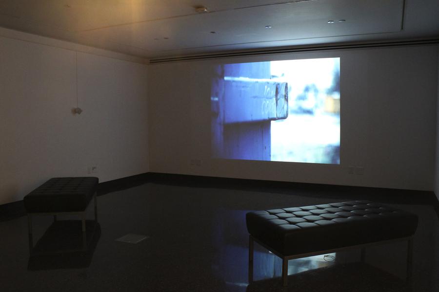 Video still in a dark room, a black leather bench in the centre