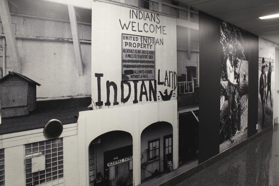 A wall covered in black and white prints. Handwritten text reads "Indians welcome, Indian land"