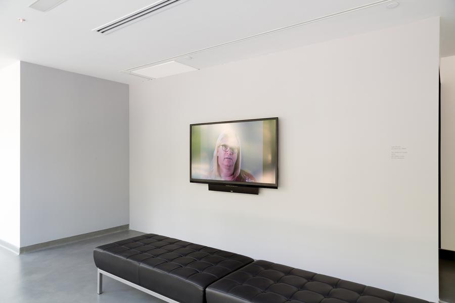 A small screen on a white wall, black leather benches in the centre of the space