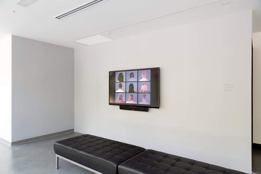 A small screen on a white wall, black leather benches in the centre of the space