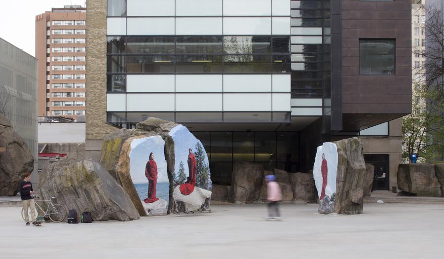 Twhree images of women in long red cloaks printed onto large rocks at Ryerson's Lake Devo, in front of Ryerson's Chang School
