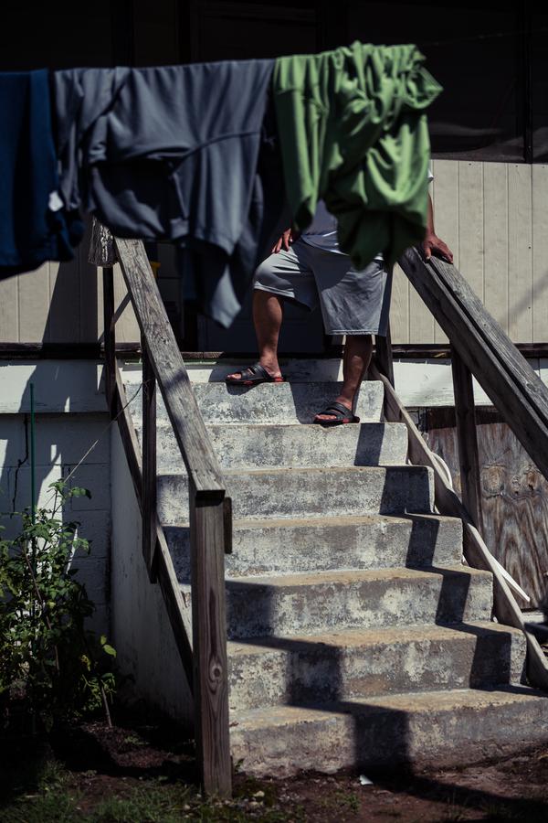 A man stands on the steps of a porch, but his face is obscured by laundry hanging on a line.