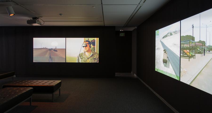 Four video screens in a dark room with a bench in the middle