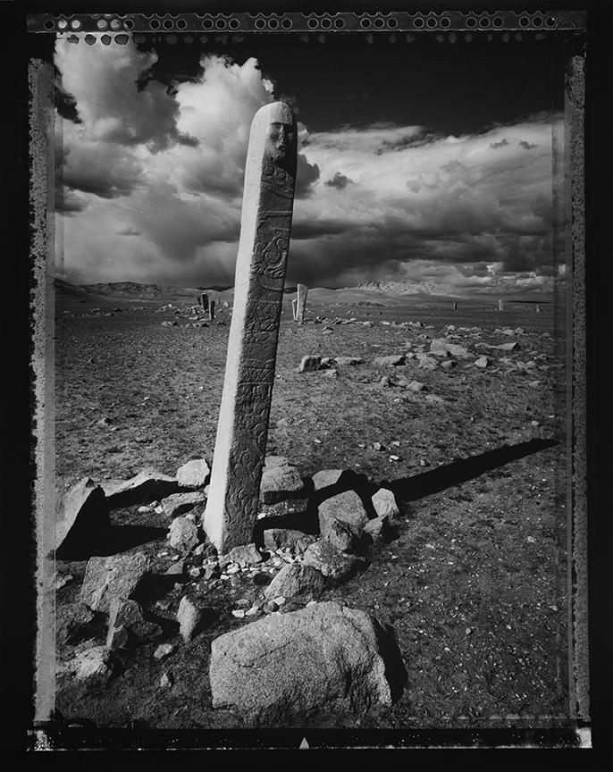 Tall thin sculpture surrounded by rocks in the middle of a desert