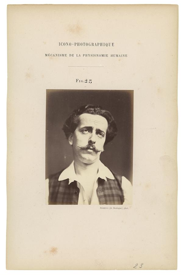 A black and white portrait of a man with dark hair and a moustache, wearing a plaid vest over a white collared shirt. He looks upwards, and looks contemplative.