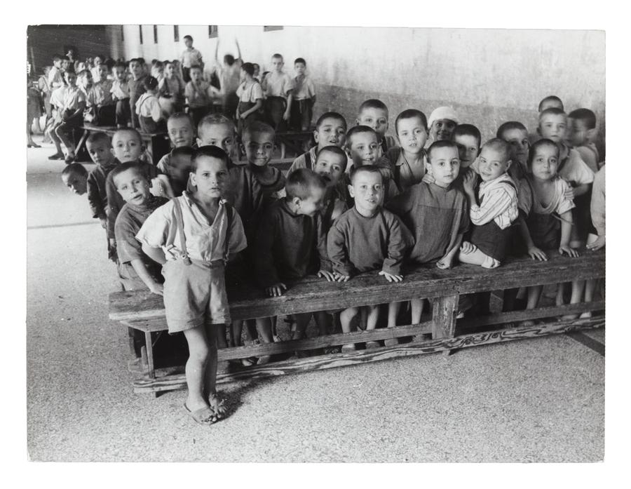 Approximately 50 children bald-headed children sit on benches
