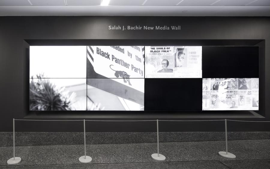 A frame from a black and white video projected on a black wall. Text on-screen reads "Black panther party"