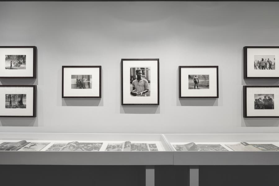 Black and white photographs in black frames hung above a white display case containing old newspapers