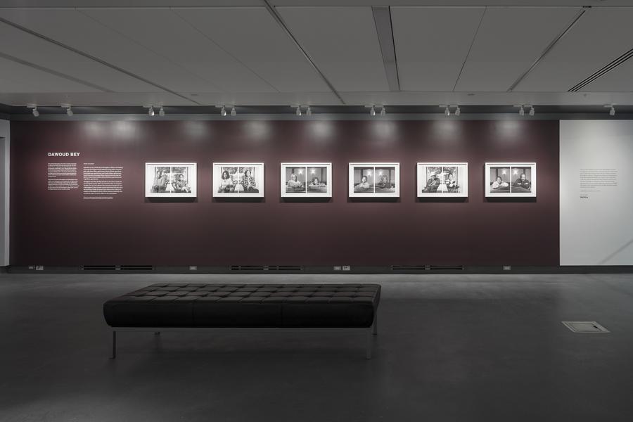 6 diptychs in white frames on a maroon wall, with a black leather bench in the foreground. Text on the wall reads "Dawoud Bey"
