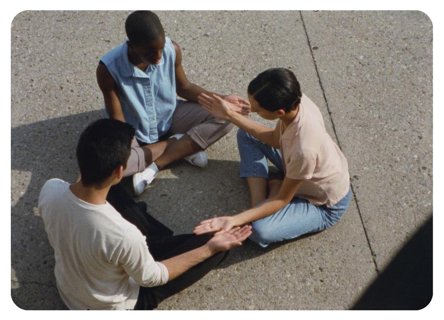 Three people sitting in a circle playing a hand game
