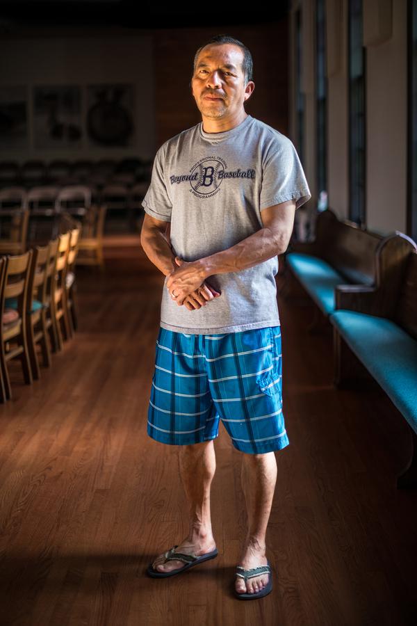 A man stands for a portrait in room with wood floors and church pews.