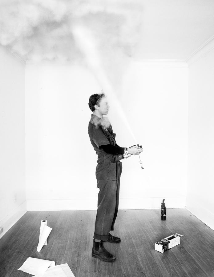 A woman in a jumpsuit sprays themselves in the face with a fire extinguisher. Haley Wilsdon, Self Defence, at the Ryerson Image Centre.
