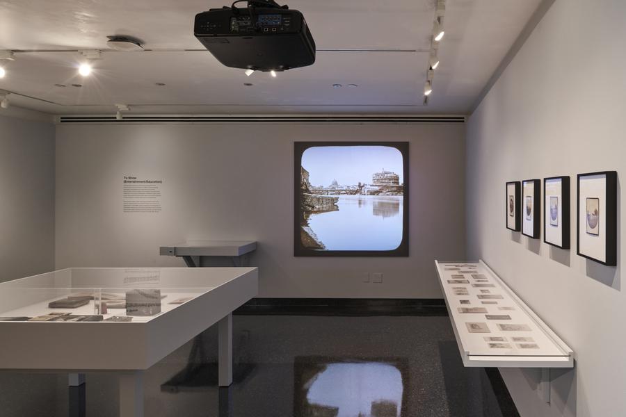 A view inside the IMC's Student Gallery with a projector, cased and framed photographs and objects.