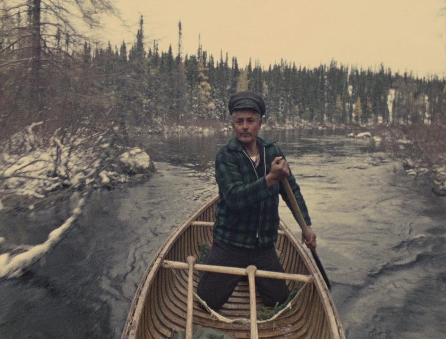 Man wearing green and black plaid and a black hat paddles a canoe