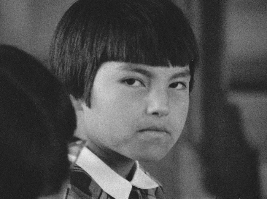 A young child with bluntly-cut black hair staring straight ahead