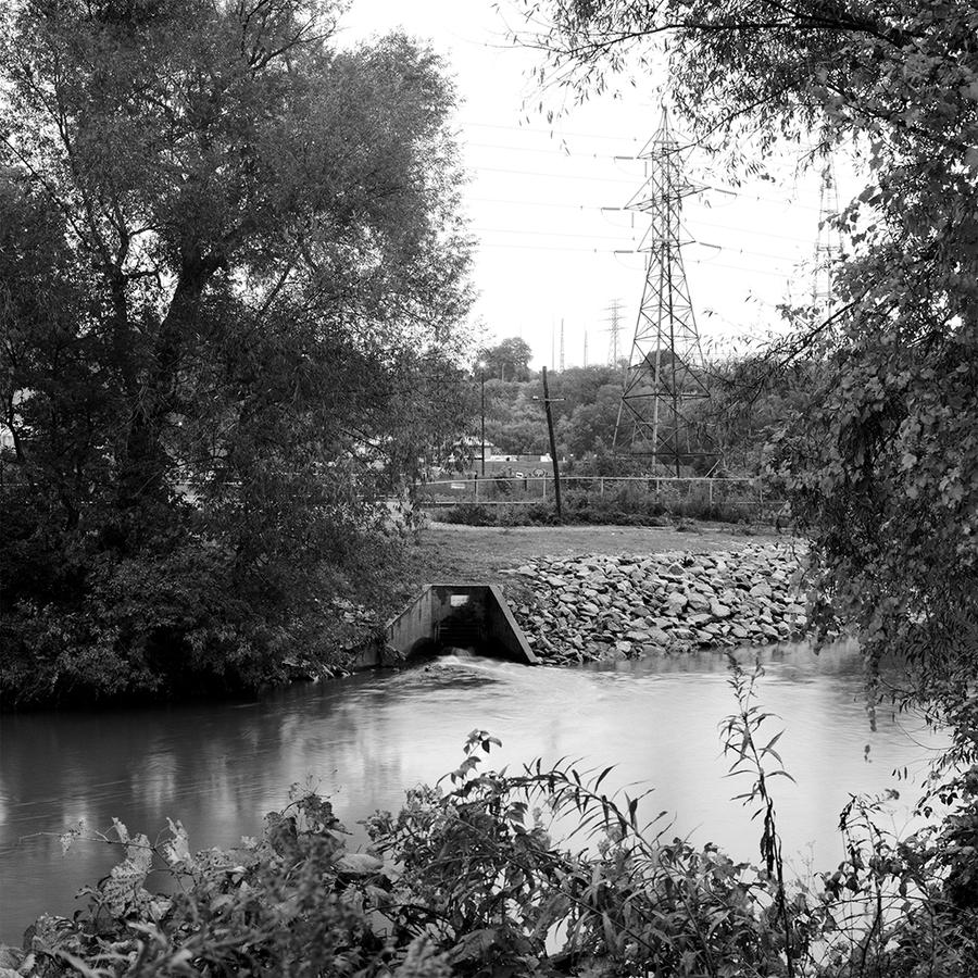 Outdoor ravine and waterway with tunnel for water pass through, surrounded by embankment of trees