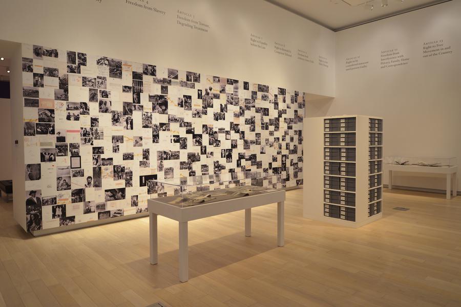 A display case in the centre of the gallery, a collage of images on the wall behind it