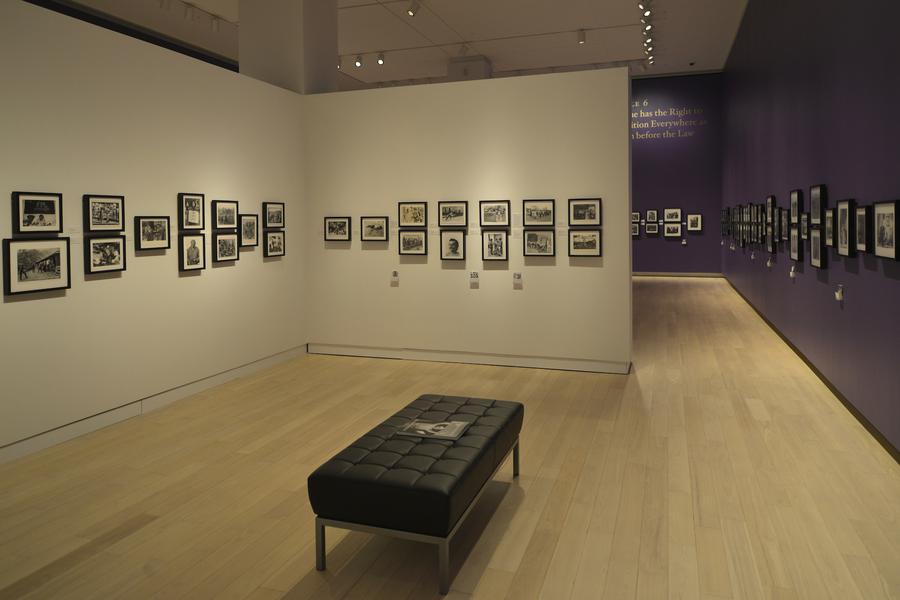 Framed photographs, white wall on the left, purple wall on the right, black bench in the center