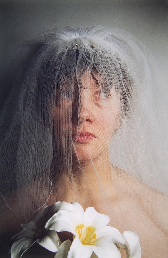 A woman wearing a white veil holds white flowers