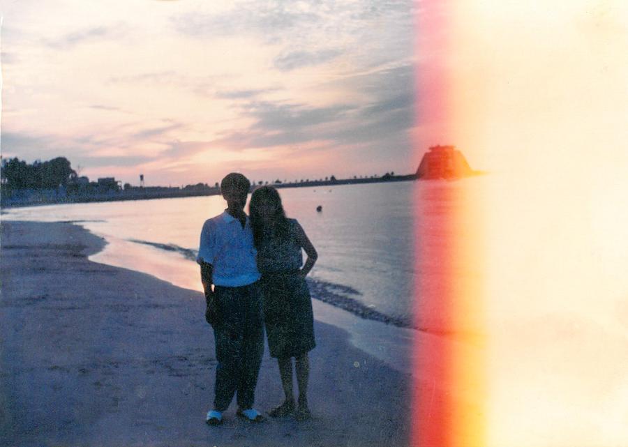 A film photograph showing two people standing on a beach as the sun sets.