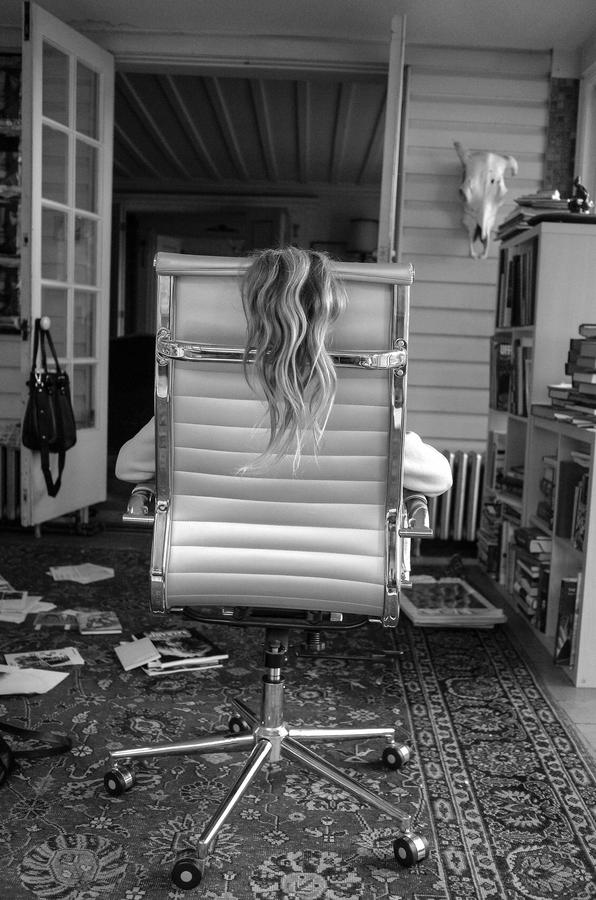 A little girl sitting in a big chair with her back towards the camera, and her hair hanging down the back of the chair