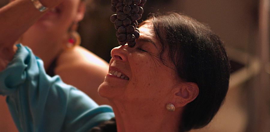 Middle-aged woman smiles with head back, eyes closed while holding grapes above face