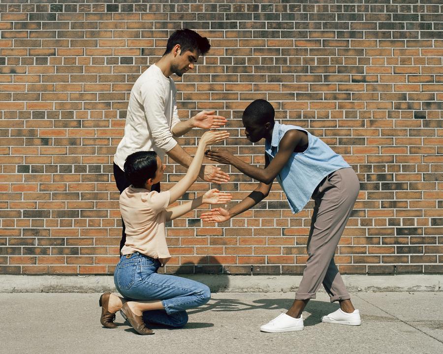 Three people in front of a brick wall playing a handgame