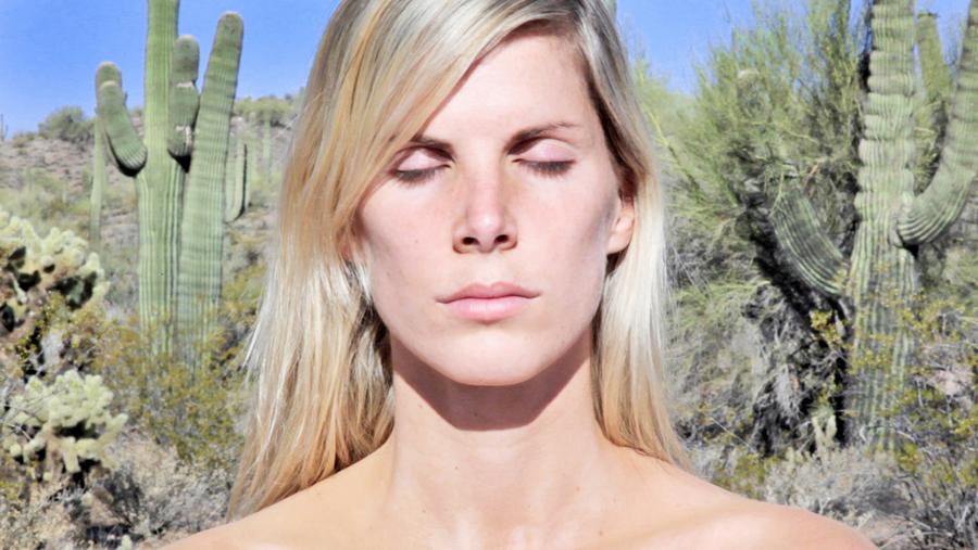 A woman with her eyes closed standing in front of a desert scene