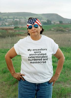 A woman stands with her hands on her hips wearing a t-shirt that says: My ancestors were annihilated, exterminated, murdered and massacred