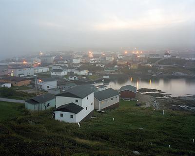 A cluster of white houses beside a body of water, the air is foggy