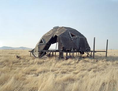 A geometric metal structure sits atop wood beams in the middle of a field