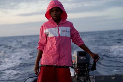 A boy on a boat on the water wearing a bright pink jacket
